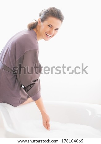 Happy young woman checking water temperature in bathtub