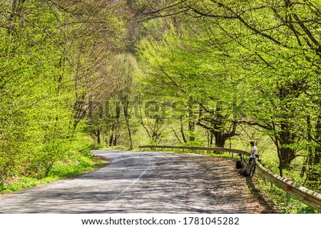 Cycle ride. Spring cycling. Green trees and grass around. Outdoor activities. The guy stopped to rest. A road with falling shadows Royalty-Free Stock Photo #1781045282