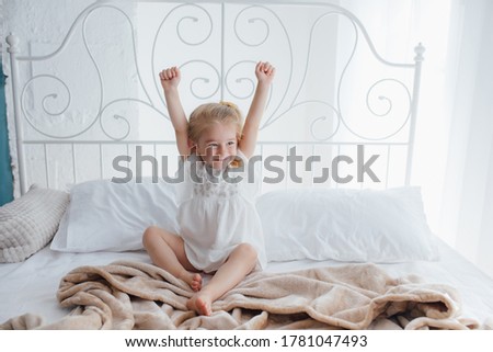 Cute little child stretching in bed, child it feels good in cozy bedroom in the morning at home