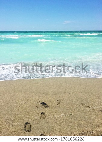 Picture of a Florida beach with footprints in the sand and bright blue water at the shore. 