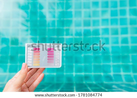 Pool tester test kit in girl hand with space on blurred clear blue swimming pool water, outdoor day light, quality tester for swimming pool water testing, pH and chlorine test
