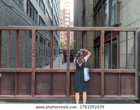a woman turned back and taking a photo of buildings. Standing between iron fence