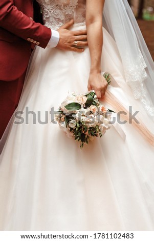 Close-up picture of bride's and groom's hands and pink flower rose bouquet.