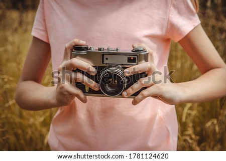 Girl taking photo outdoors with old film camera. Selective focus at lens, unrecognizable person. 