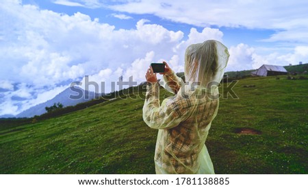 Woman tourist in a yellow raincoat taking photo on a phone camera mountain landscape during a trip to the mountains          