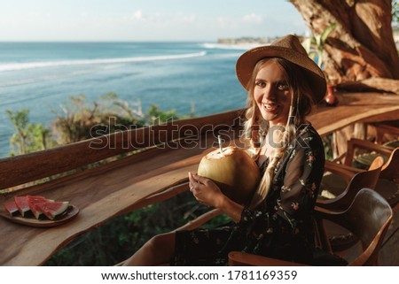 Portrait of attractive young woman drinking coconut juice, smile and look at the camera, enjoy tropical beach vacation