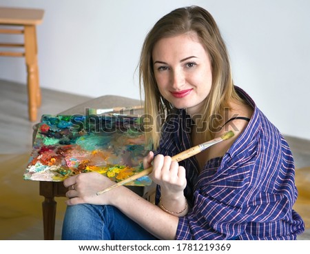 young beautiful woman artist drawing a picture with a palette of paints in hands.