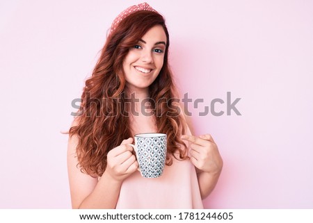 Young beautiful woman holding coffee smiling happy pointing with hand and finger 