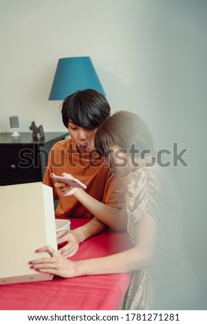 Asian thai couple taking picture of pizza in the box. Eating food in dinning room.