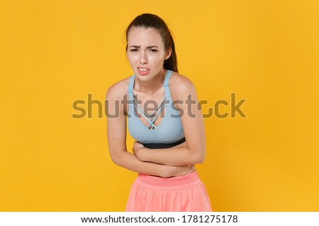 Sick young fitness sporty woman girl in sportswear posing working out isolated on yellow wall background studio portrait. Workout sport motivation concept. Having abdominal pain, put hands on stomach Royalty-Free Stock Photo #1781275178