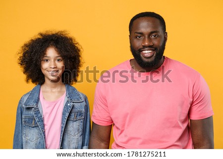 Smiling african american guy girl brother sister in denim pink clothes posing isolated on yellow wall background studio portrait. People emotions lifestyle concept. Mock up copy space. Looking camera