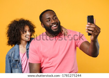 Funny african american guy girl brother sister in denim pink clothes isolated on yellow background studio portrait. People lifestyle concept. Mock up copy space. Doing selfie shot on mobile phone
