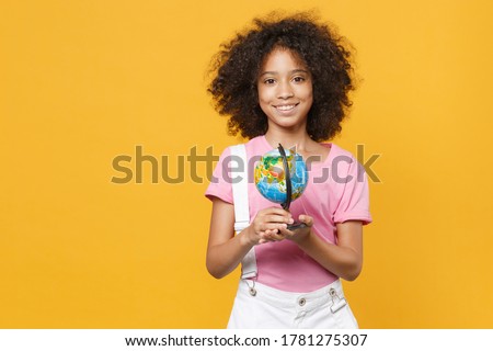 Pretty little african american kid girl 12-13 years old in pink t-shirt isolated on yellow background children studio portrait. Childhood lifestyle concept. Mock up copy space. Hold Earth world globe