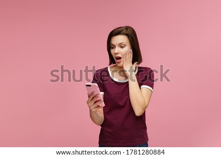 Surpised young brunette woman holding pink smartphone, smiling and expressing positivity. Happy girl got shocking positive news. Copy space. Young people working with mobile devices. Royalty-Free Stock Photo #1781280884