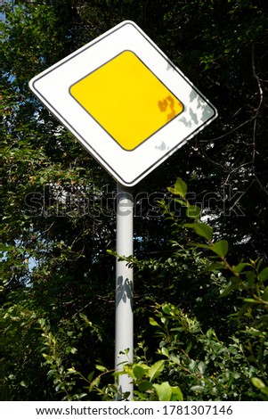 Road sign main road. A road sign on a gray post at the edge of the road among the foliage of trees.