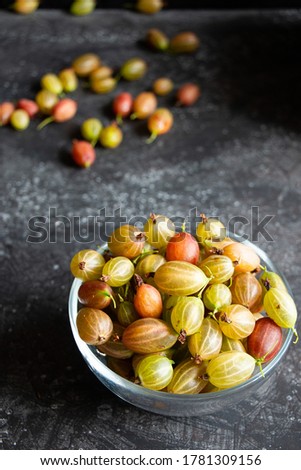 Glass bowl with ripe gooseberries on a dark background close-up. Healthy food and harvest concept.