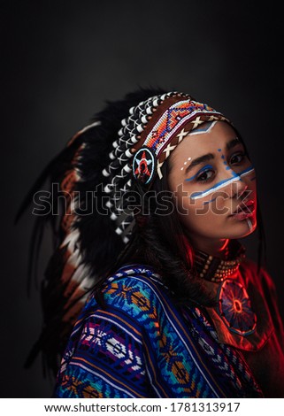 Portrait of a beautiful American Indian woman in ethnical costume and traditional make up. Studio portrait on a dark background