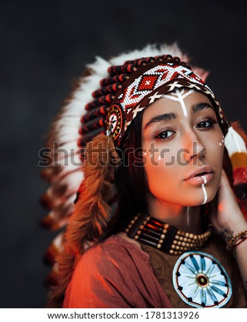 Portrait of a beautiful American Indian woman in ethnical costume and traditional make up. Studio portrait on a dark background