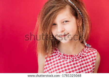 Little blonde girl in red checkered dress smirking, isolated on pink background