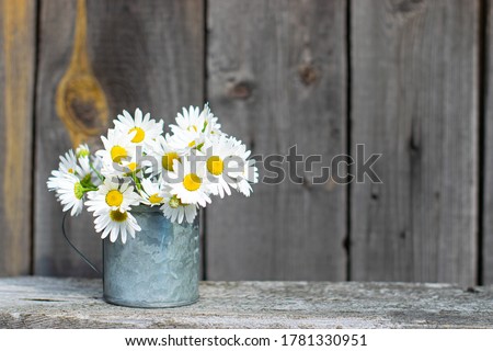 a bouquet of daisies in a metal mug stands on a wooden table, rustic style