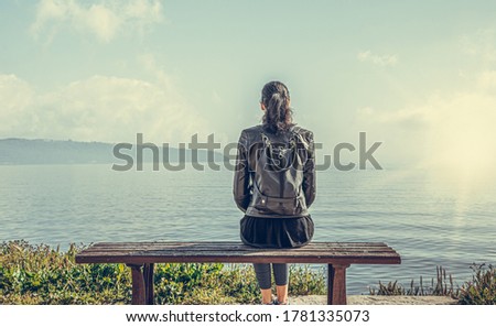 A lonely woman sits on a bench by the water. Toned image.