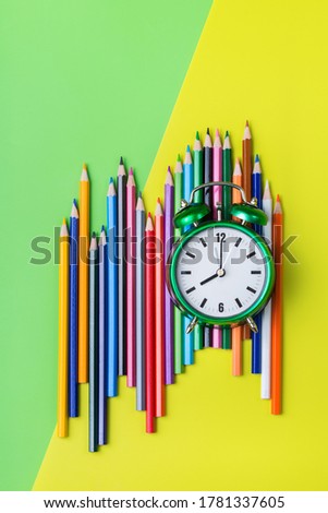 Assortment of colourful rainbow pencils and alarm clock on a mint green and yellow background. Top view flat lay. Back to school concept