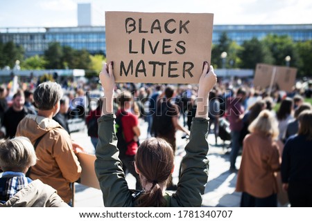Rear view of black lives matters protesters holding signs and marching outdoors in streets.