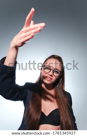 A young girl 20-25 years old in glasses, a jacket and with a tail in the image of a teacher poses on a gray background and shows different emotions.