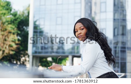 Young afro american woman in white shirt outdoors in the city against business building.