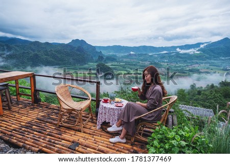 Portrait image of a beautiful woman drinking hot coffee on balcony with mountains and green nature background