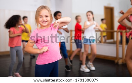 Portrait of little girl doing exercises during group class in dance center