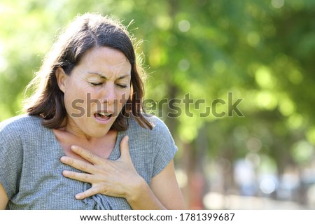 Middle age woman wheezing holding chest standing in a park at summer Royalty-Free Stock Photo #1781399687