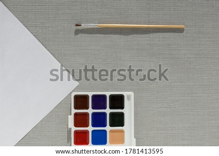 Brush, pallet watercolor paint and empty sheet of paper on grey background. no people. Top view. copy space. Workplace artist. drawing kit. fine art, creativity, painting and artistic tools concept