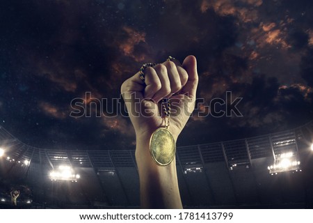 Champion. Award of victory, male hands tightening the golden medal of winners against cloudy dark sky. Sport, competition, championship, winning, achieving the goal. Prize for success and honor. Royalty-Free Stock Photo #1781413799