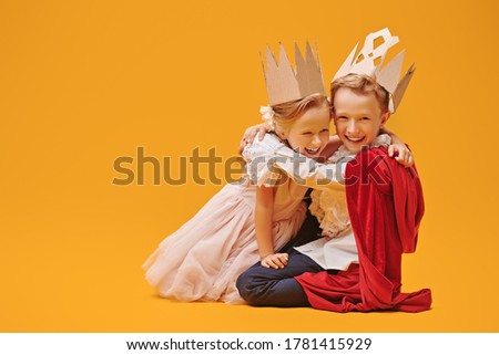 A boy and a girl in Prince and Princess costumes laugh and hug. Childhood dreams. Fantasy, imagination. Studio portrait on a yellow background. Royalty-Free Stock Photo #1781415929