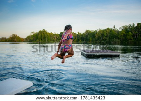 Little girl jumping into a lake enjoying her summer holiday at the cottage.