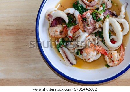 Picture of stir-fried hot and spice sweet basil with seafood, a large dish for up to four people, served on a plate, and placed on a wooden background.