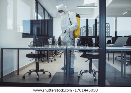 Office disinfection during COVID-19 pandemic. Man in protective suit and face mask spraying for disinfection in the office Royalty-Free Stock Photo #1781445050