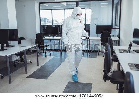 Office disinfection during COVID-19 pandemic. Man in protective suit and face mask spraying for disinfection in the office Royalty-Free Stock Photo #1781445056