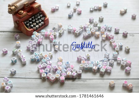 Selective focus of miniature typewriter,alphabet beads and paper written with Subtitle on white wooden background.