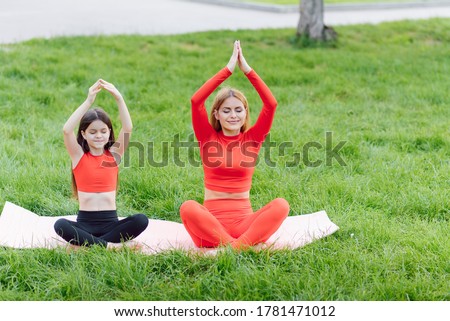Mother and daughter doing yoga exercises on grass in the park at the day time