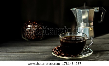 Hot coffee in a coffee cup and roasted coffee beans with a dark tone wood floor. And there is a copy space.