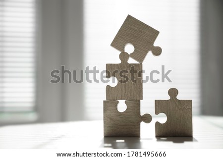 4 Four brown pieces of puzzle stand on wooden table on office window background. empty copy space for inscription or objects. idea, sign, symbol, concept of connecting. blinds on the window