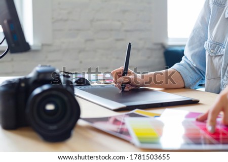 Close up portrait of graphic designer hands retouching images using graphic drawing tablet in special program. Laptop,monitor, and color palette. Retoucher workplace in photo studio. Creative agency.