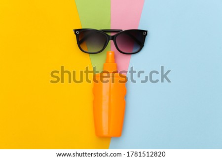 Beach vacation. Sunblock bottle and sunglasses on colored background. Top view. Flat lay