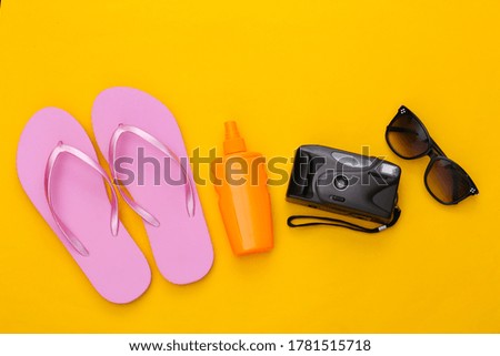 Beach vacation, travel concept. Sunblock bottle, sunglasses, flip flops and camera on yellow background. Top view. Flat lay