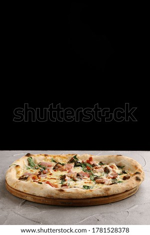 pizza with meat, mushrooms and spinach close up on gray concrete or stone table and black background for copy space