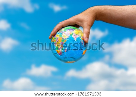 Human hand is holding small globe  Travel and global issues concept.Blue sky and white clouds.Background copy space for your text