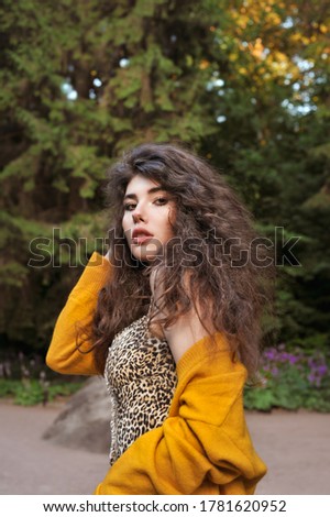 Young brunette girl with curly hair. Curly girl walks in the park.
