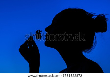 silhouette of a girl with her hair up, smelling a flower on a blue background